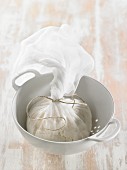 How to prepare vegan macadamia nut cheese: cheese mix being dried in a muslin cloth in a colander