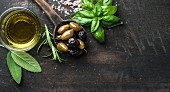 Green and black Mediterranean olives in old cooking spoon with olive oil and herbs
