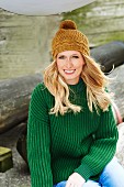 A blonde woman wearing a green knitted jumper and mustard-yellow knitted bobble hat