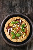 Homemade vegetable open pie galette with colorful tomatoes, tomato pesto, feta cheese and fresh basil