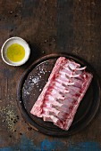 Raw uncooked rack of lamb on wood chopping board with salt, pepper, dry herbs and olive oil