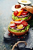 Tasty homemade sandwiches with avocado, tomato, onion and pepper on a slate board