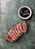 Sliced grilled Tuna steak in sesame and soy sauce on stone slate board