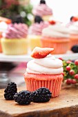 A pink strawberry cupcake with blackberries