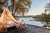 Lounger under mosquito net on edge of pool with panoramic view