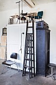 Schwarze Leitern und verschiedene Stühle auf weißem Holzschrank in aufgeräumter Werkstatt