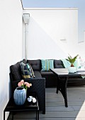 Black corner sofa with colourful scatter cushions against white wall on summery terrace