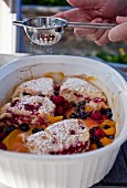 Peach, raspberry and blueberry cobbler being dusted with icing sugar