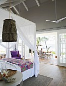 View past canopy bed onto terrace of summery beach house