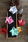 Colourful origami stars on chalkboard and pine cones on wooden surface