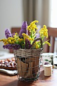 Gelb-violetter Blütenstrauss in Drahtkorb als Tischdekoration