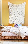 Cream fringed rug hung on yellow wall above bed