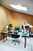 Vintage beer table used as desk with stacked books and retro upholstered office chair in attic study