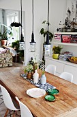 Ceramic bowls and vases of flowers on rustic table below industrial-style pendant lamps