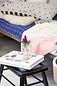 Book and flower in water glass on black stool next to comfortable wooden couch