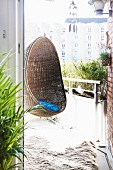Gemütlicher Korb-Hängesessel auf sommerlichem Balkon