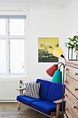 Blue-upholstered couch next to retro standard lamp and chest of drawers