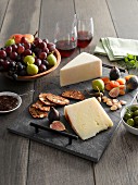 A cheeseboard with fruit, pistachios, fruitcake and olives