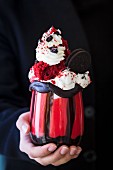 A woman holding a red velvet freak shake with Oreo biscuits