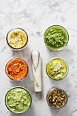 Assorted jars of pesto on a marble surface with a pestle