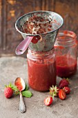 Strawberry jam in a glass jar with a funnel