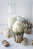 Easter egg and thyme in metal crown next to quail eggs