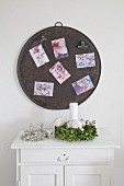 Postcards on round metal sheet used as magnetic pinboard above wreath of box