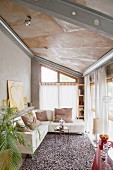 Gemütliche Ledercouchgarnitur mit Kissen in hellem Wohnbereich mit Dachschräge und Stahlträgern