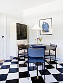 Runder schwarzer Tisch mit blauen Stühlen auf schwarz-weißem Schachbrettmusterboden