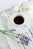 A cup of coffee and lavender flowers on a wooden table
