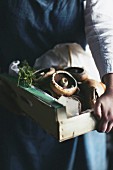 A chef carrying a wooden box of mushrooms and herbs