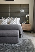 Bed with upholsered headboard in bedroom in shades of grey