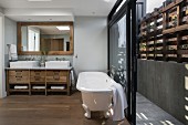 White, free-standing bathtub in front of open sliding doors leading to narrow courtyard with rustic wooden screen