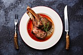 Roasted beef ribs on bone on plate with knife and fork carving set on dark background
