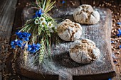 Healthy wholemeal bread rolls with ears of corn and field flowers on a wooden board