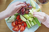 Kinderhände nehmen Obst und Gemüse von einem Teller