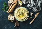 Hummus with lemon, herbs and a baguette on a rustic wooden board