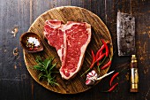 Rohes T-Bone-Steak, Gewürze und Küchenbeil auf Holzuntergrund