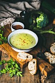 Fresh homemade pea, broccoli, zucchini cream soup in white bowl with fresh baguette slices and parsley