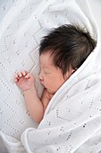Newborn baby girl asleep in white blanket