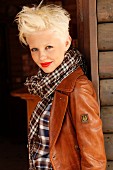 A blonde woman wearing a checked blouse, scarf and brown leather jacket