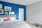 Blaue Schlafzimmerwand mit Bildergalerie neben grafischem Tapetenmuster