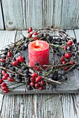 Red pillar candle in wreath of sloe branches and rose hips