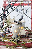 Candle lantern with punched stars amongst sloe branches on red chair