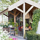 Blick in halboffenes Gartenhaus mit verschiedenen Topfpflanzen und Blumenampeln