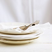 A stack of white plates with napkins and cutlery