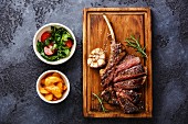 A grilled veal chop with potato wedges and tomato and rocket salad