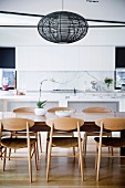 Wooden chairs around the dining table with rattan lamp in front of the open kitchen