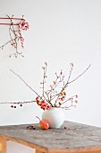 Zweige mit Zieräpfeln in Vase und eine Birne auf Holztisch, Zuckerstange an Garderobe