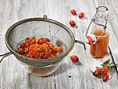 Rose hip juice in a bottle with pitted and boiled rose hips in a strainer